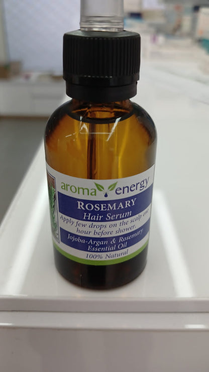 A bottle of Aroma Energy Rosemary Hair Serum with a dropper, on a tabletop.